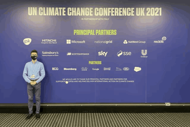 a man wearing a mask stands in front of a sign for the un climate change conference uk 2021