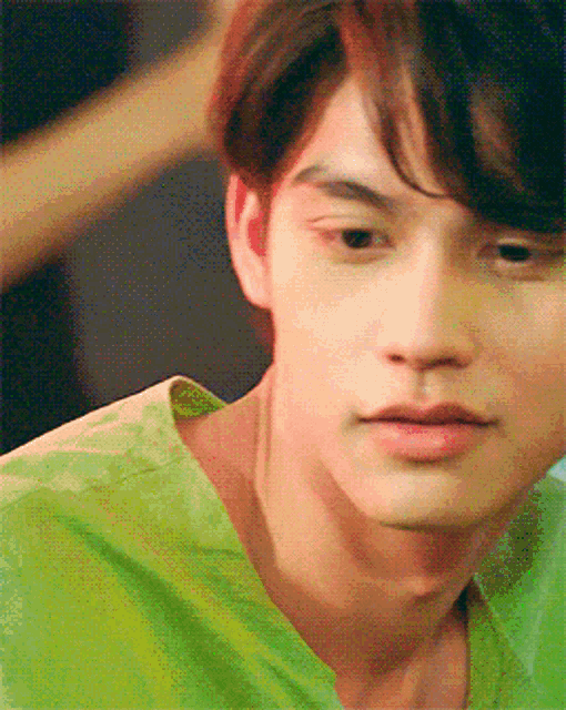 a close up of a young man 's face with a green shirt on