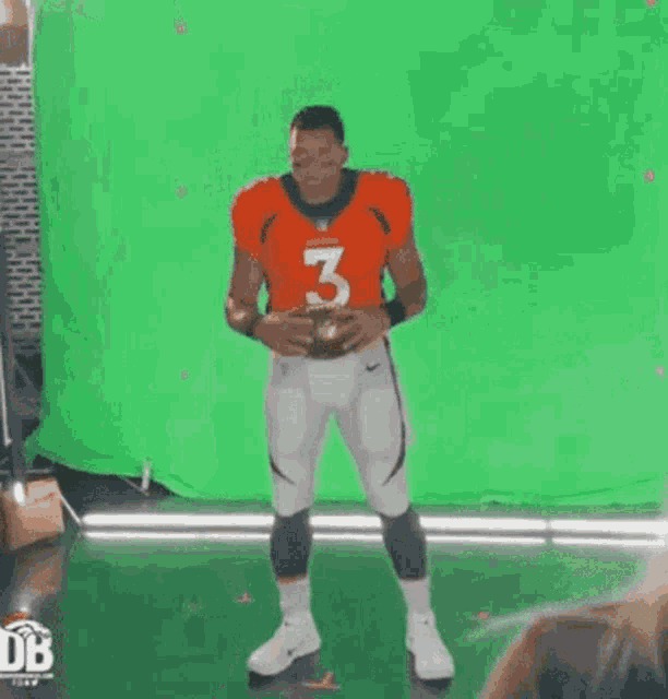 a football player is standing in front of a green screen and holding a football .