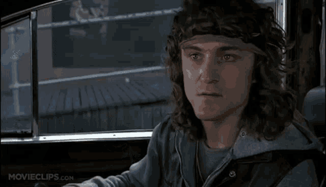 a man with long curly hair and a headband is sitting in a car looking out the window .