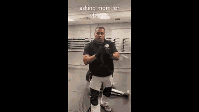 a man in a black shirt and white shorts is standing in a gym with his hands folded in front of his face .