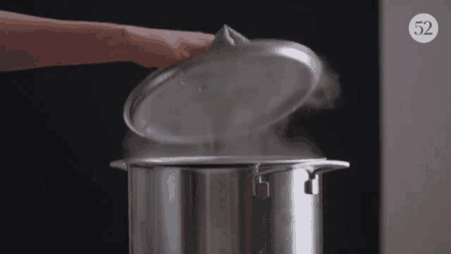 a person is holding the lid of a pot of boiling water .