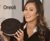 a woman is smiling while holding a large oreo cookie .