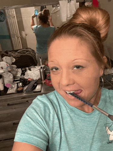 a woman is brushing her teeth in front of a mirror and wearing a shirt that says under armour