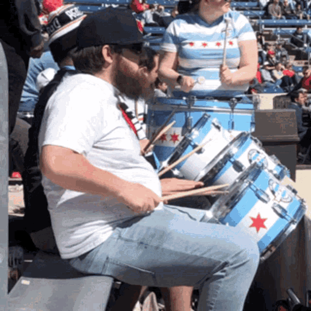 a man sits on a bench playing a drum set with chicago flags on them
