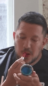 a man is applying lipstick to his lips in front of a mirror .