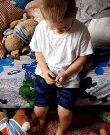 a little boy is sitting on a bed with a teddy bear and a blanket that says ' a ' on it