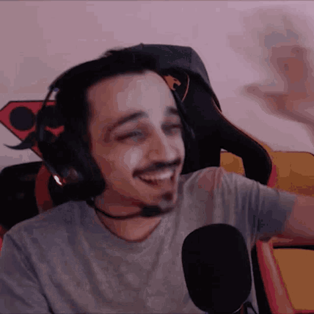 a man wearing headphones and a microphone is smiling while sitting in a chair .