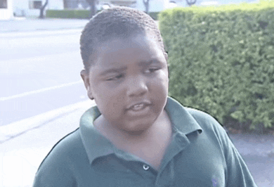 a young boy wearing a green polo shirt looks at the camera with his eyes closed