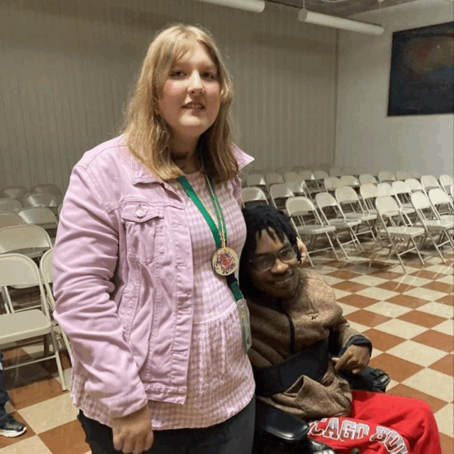 a woman in a pink jacket is standing next to a man in a wheelchair wearing a shirt that says clash