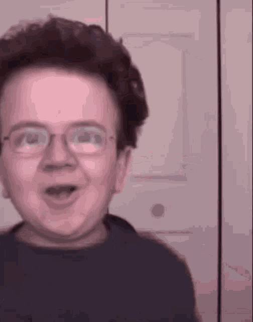 a young boy wearing glasses is making a funny face in front of a door .