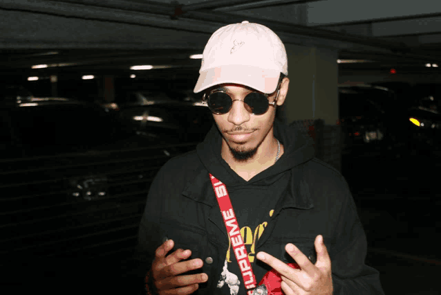 a man wearing a pink hat and sunglasses has a red supreme lanyard around his neck