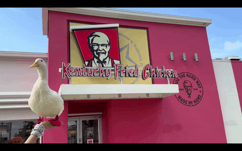 a white duck stands in front of a pink kentucky fried chicken restaurant