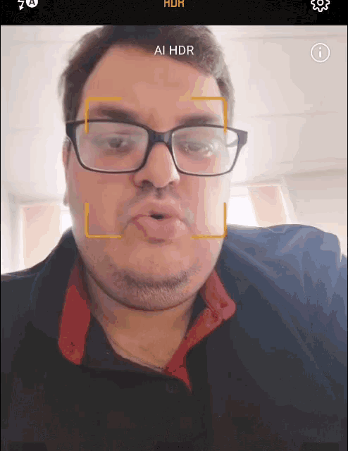 a man wearing glasses is taking a selfie and the screen says ai hdr on it