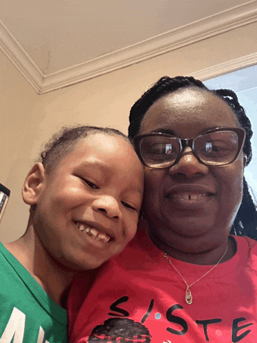 a woman wearing glasses and a red shirt that says sister smiles with a child