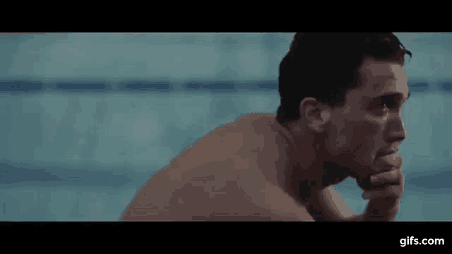 a shirtless man is sitting next to a swimming pool with his hand on his chin .