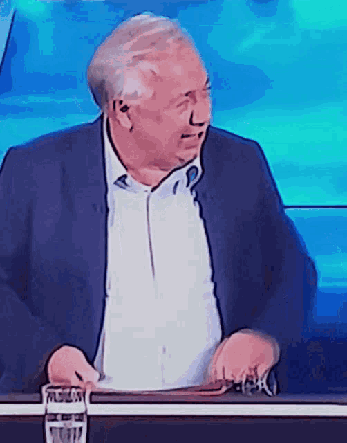 a man in a suit and white shirt is sitting at a table with a glass of water in front of him