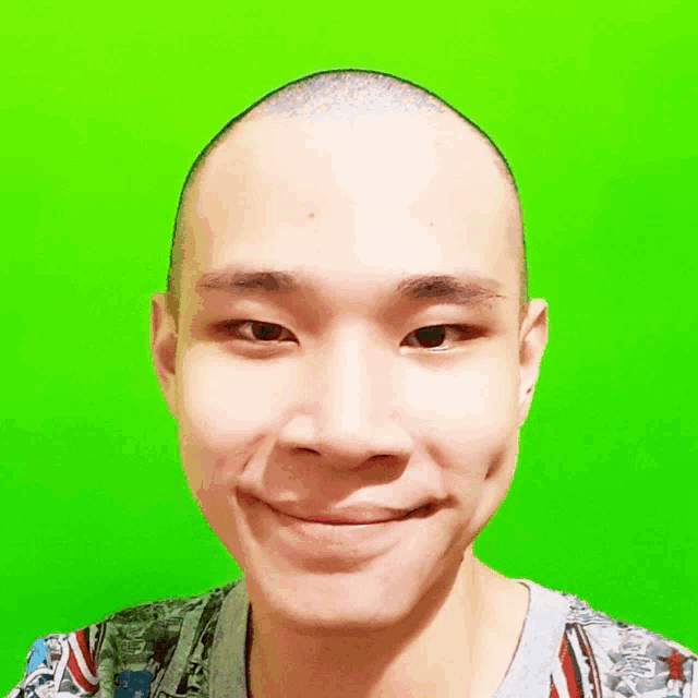 a young man with a shaved head is smiling in front of a green background