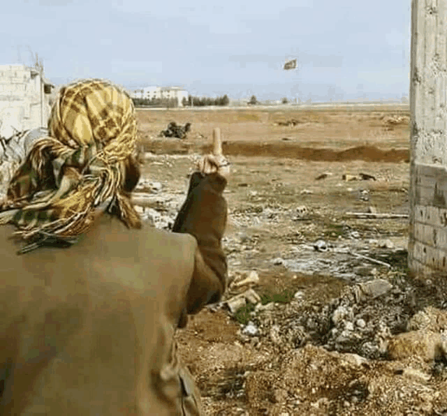 a man wearing a head scarf is pointing at a flag flying in the distance