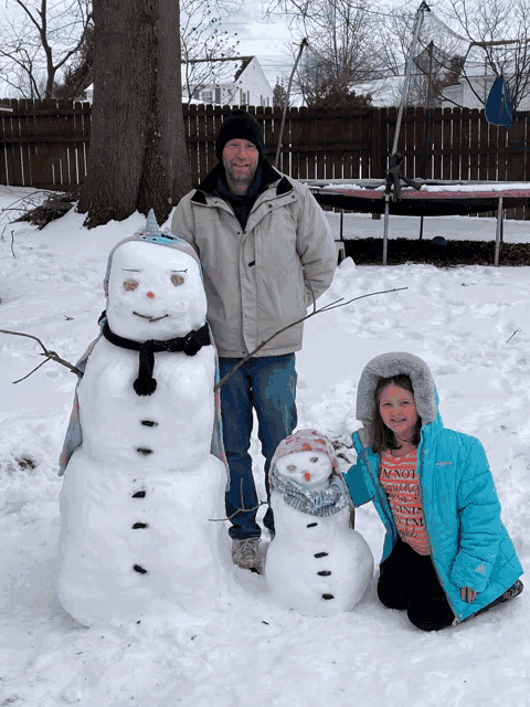 a man and a girl are posing with their snowmen