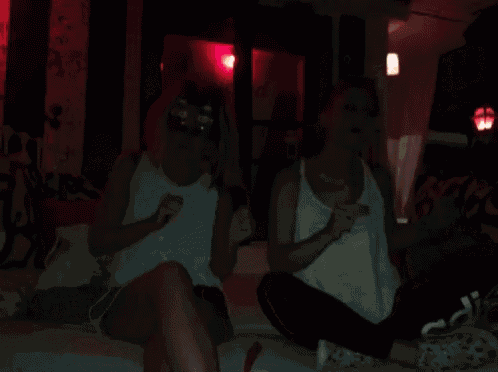 two women are sitting on a bed with one wearing a headband that says ' a ' on it