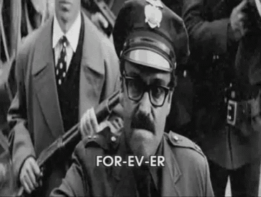 a black and white photo of a police officer holding a gun in front of a crowd of people .