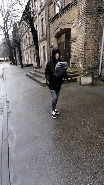 a person carrying a baby in a sling walks down a street