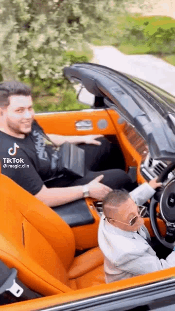 a man is driving a convertible car with a child sitting in the back seat .