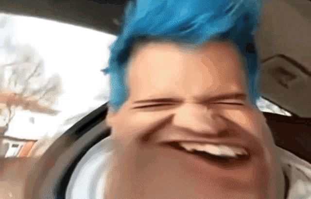 a man with blue hair is making a funny face while sitting in the back seat of a car .