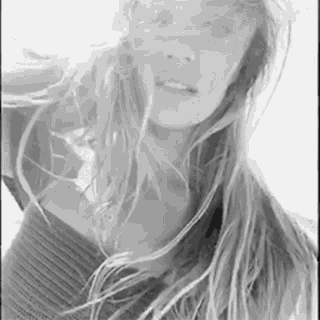 it is a black and white photo of a woman with long hair blowing in the wind .