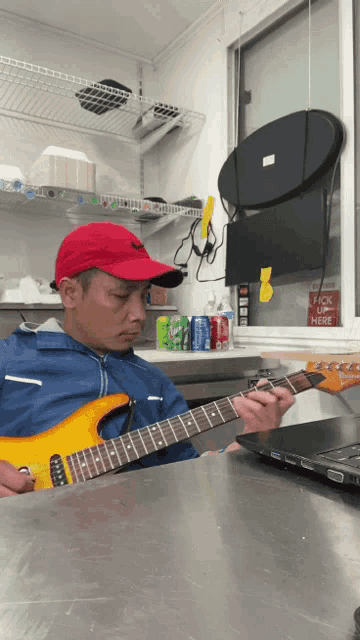 a man in a red hat is playing a guitar in front of a window that says " pick up here "