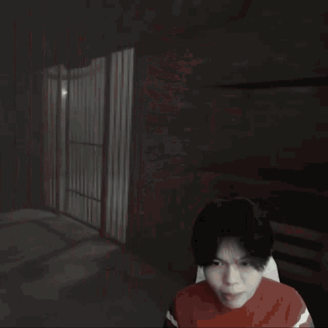 a young man in a red shirt is sitting in front of a prison cell with bars .