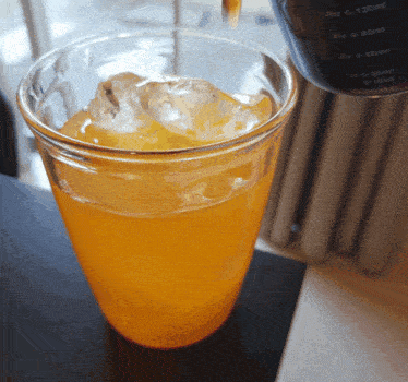 a plastic cup filled with orange liquid and ice sits on a black table