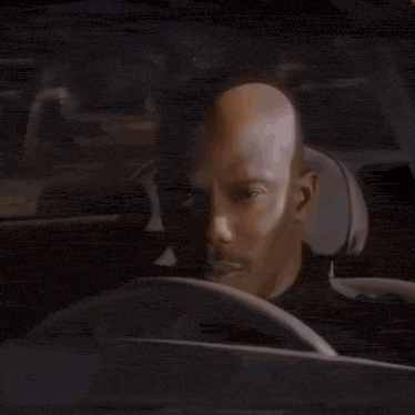 a man with a bald head is driving a car and looking at the camera