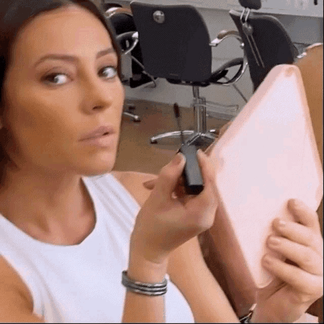 a woman is applying lipstick in front of a mirror in a hair salon .