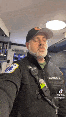 a man with a beard wearing a black jacket and a hat with a patch on his arm that says emergency medical technician