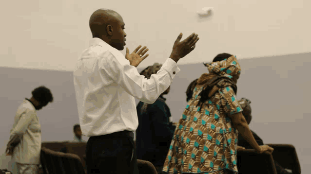 a man in a white shirt is standing in front of a group of people with his hands in the air