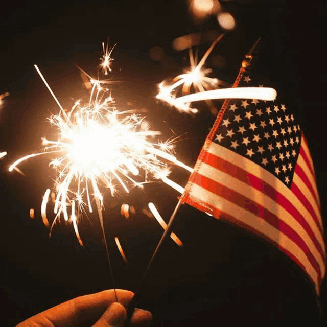 a person is holding a small american flag in front of sparklers