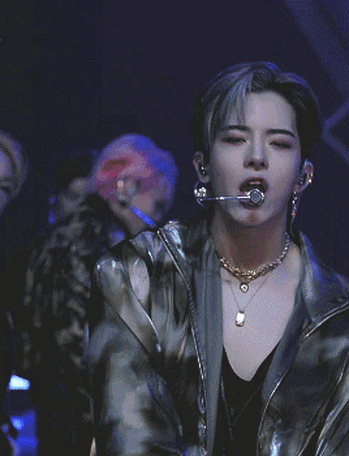 a young man with a microphone in his mouth is wearing a necklace
