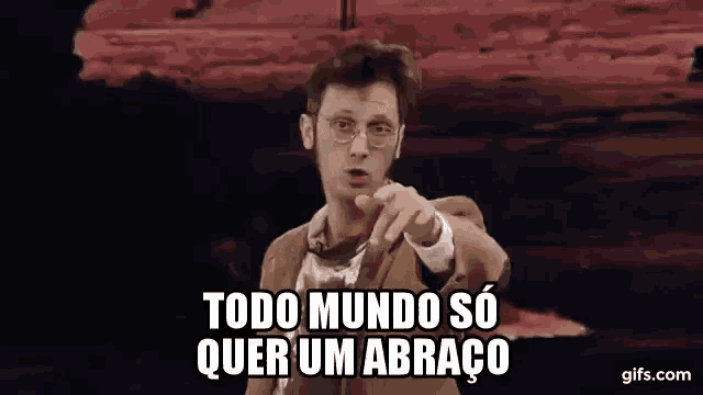 a man in a suit and glasses is pointing at the camera with the words todo mundo so quer um abraço written below him .