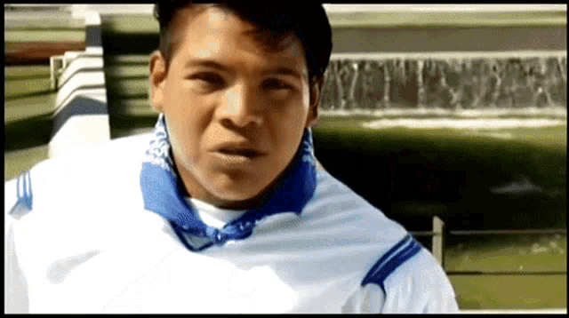a man wearing a white shirt with blue stripes on the sleeves stands in front of a waterfall