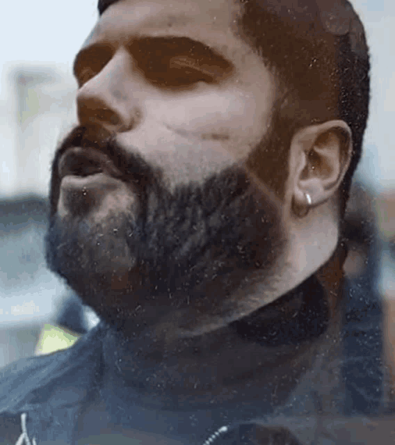 a close up of a man with a beard and earrings looking up .