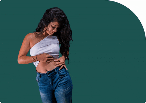 a woman in a white top and blue jeans looks down at her stomach