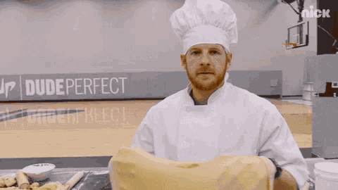 a man in a chef 's hat is holding a piece of dough in front of a basketball court .