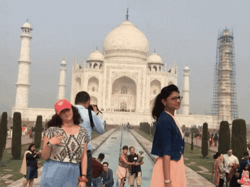 a woman wearing a red hat that says ' donald trump ' on it is standing in front of the taj mahal