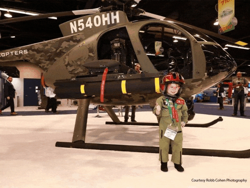 a boy in a helicopter costume stands in front of a helicopter with the number n540hh on the side