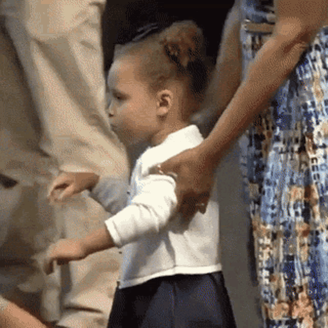 a little girl in a white shirt and blue skirt is being held by a woman in a blue dress .