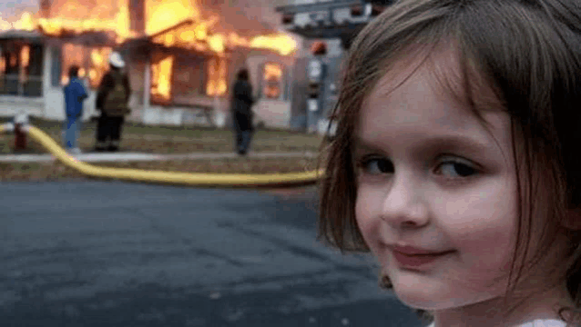 a little girl is standing in front of a burning house and smiling .