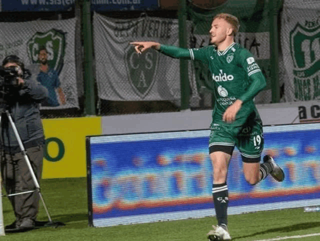 a soccer player wearing a green aldo jersey is running on a field