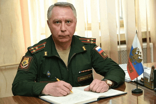 a man in a military uniform sits at a desk in front of a flag that says " russia "